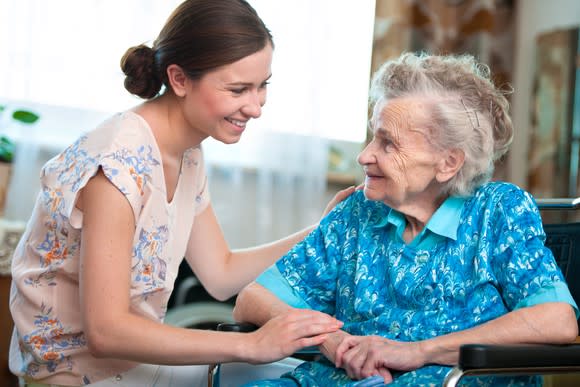 A senior woman sits next to a younger woman resting a hand on her arm and another on her back.