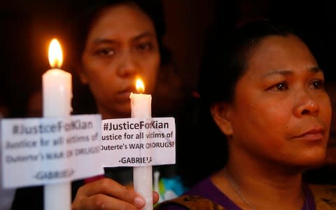 Protesters display placards and candles outside the wake for slain Delos Santos - Credit: AP