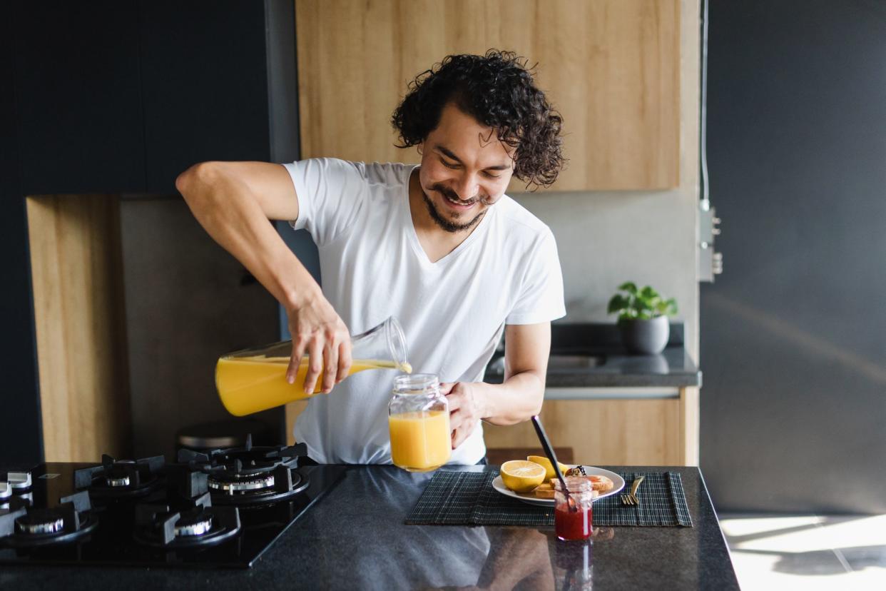 young latin man preparing and eating a healthy breakfast with fruit orange juice, pineapple and toast bread at home in Mexico Latin America, hispanic people