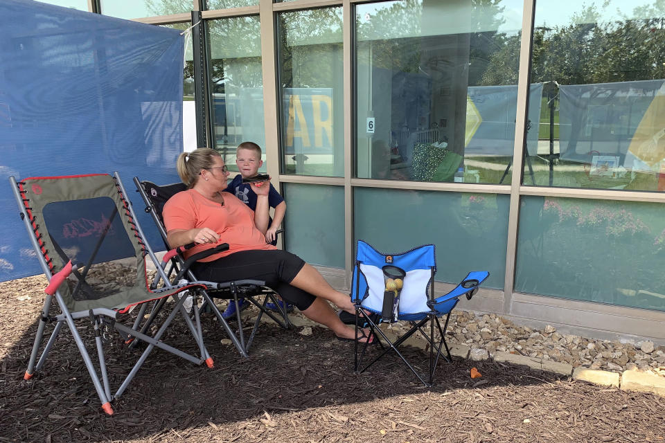 Billie Barker with her son Brody, 6, uses her cellphone to speak with her husband, Daryl, who is on the other side of the window inside his room at Lake Regional Hospital in Osage Beach, Mo., on Monday, July 26, 2021. It was the 17th day the 31-year-old spent in the ICU battling COVID-19 as cases continue to rise across the state. (AP Photo/Sarah Blake Morgan)