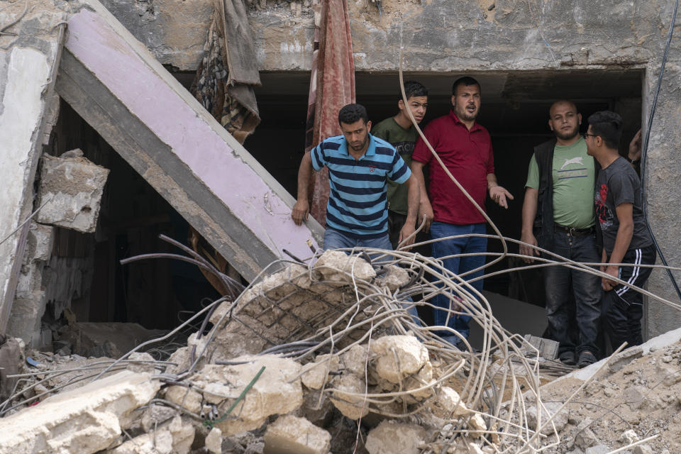 Ramez al-Masri, 39, third from right, stands inside a severely damaged building beside the crater where his home was destroyed by an air-strike prior to a cease-fire reached after an 11-day war between Gaza's Hamas rulers and Israel, Sunday, May 23, 2021, in Beit Hanoun, the northern Gaza Strip. (AP Photo/John Minchillo)