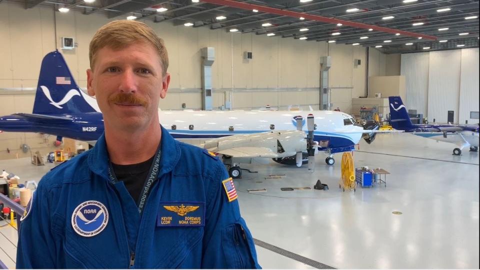 NOAA Commissioned Officer Corps. Lt. Cmdr. Kevin Doremus stands inside a Lakeland hangar with WP-3D Orion "Kermit" in the background.