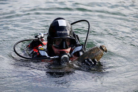 A diver from a bomb-disposal unit gies up the surface an unexploded shell recovered in the Meuse River at Sivry-sur-Meuse, close to WWI battlefields, near Verdun, France, October 23, 2018 before the centenial commemoration of the First World War Armistice Day. REUTERS/Pascal Rossignol