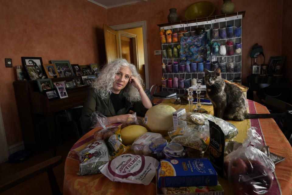 Phyllis Marder poses with her cat, Nellie, with food she recently obtained from a local food bank in the dining room of her home in Evanston, Ill., on Thursday, Nov. 5, 2020. At first, Marder, 66, didn’t tell anyone about going to food pantries. Then she had a change of heart. “Keeping a secret makes things get worse,” she says ’”… and makes me feel worse about myself, and so I decided that it was more important to talk about it." (AP Photo/Charles Rex Arbogast)