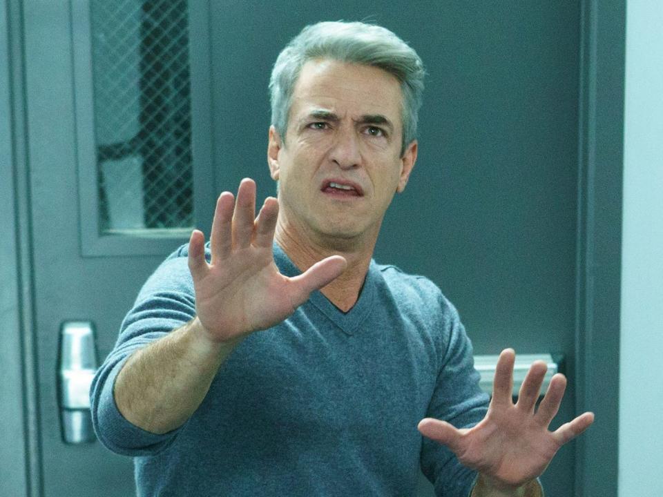 Dermot Mulroney holds his hands out and looks confused at the bottom of a stairwell on the set of "New Girl"