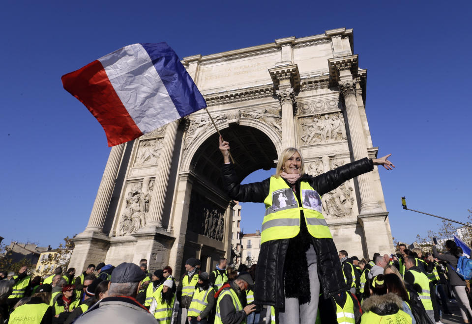 A demonstrator wearing her yellow vest waves a national flag during a protest in front of the Arc de Triomphe of the Porte d'Aix, in Marseille, southern France, Saturday, Dec. 29, 2018. The yellow vest movement held several peaceful demonstrations in cities and towns around France, including about 1,500 people who marched through Marseille. (AP Photo/Claude Paris)