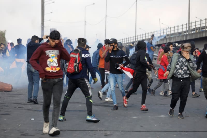 Iraqi demonstrators run away from tear gas during ongoing anti-government protests, in Baghdad