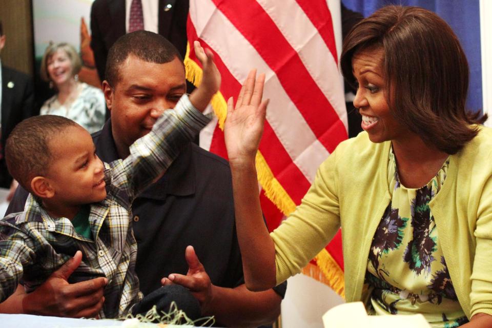 First lady Michelle Obama gets a high five with Eun White, seated with his father, Army Maj. Eunotchol White, during the first lady's visit to Fisher House at Walter Reed National Military Medical Center in Bethesda, Md., Wednesday, April 4, 2012. The Fisher House program houses military families while a family member is receiving medical care. (AP Photo/Jacquelyn Martin)