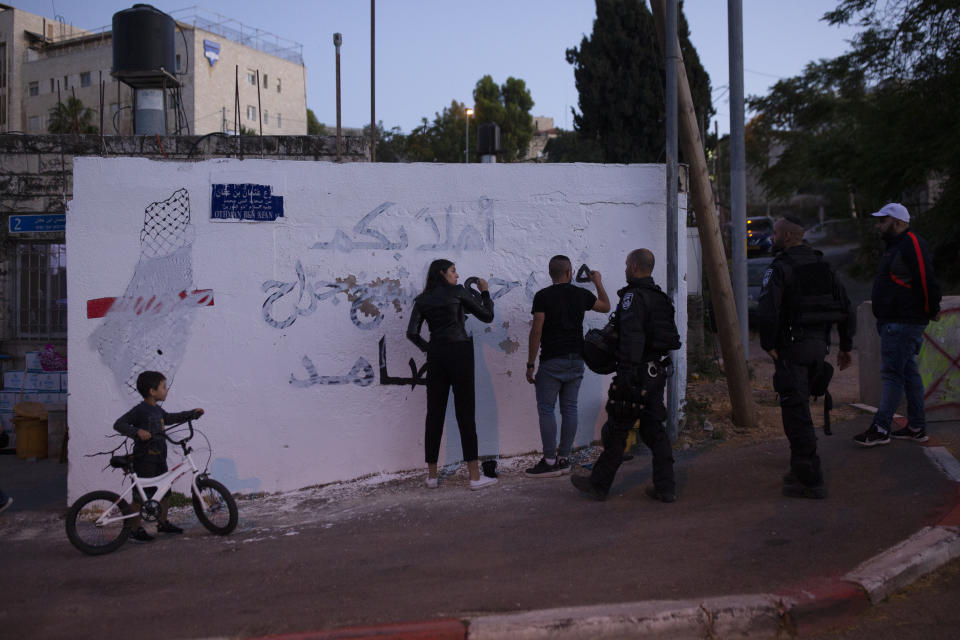 FILE - In this May 24, 2021, file, photo, Palestinian activists are approached by Israeli police as they repair a mural that was defaced by a Jewish settler in the Sheikh Jarrah neighborhood of east Jerusalem, where Palestinian families face imminent eviction from their homes by Israeli settlers. The activist at right was arrested after re-painting the Arabic phrase: "welcome to the resilient neighborhood of Sheikh Jarrah."(AP Photo/Maya Alleruzzo, File)