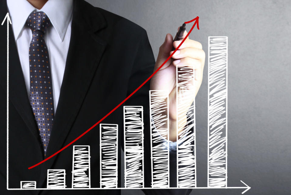 A man in a suit holding a pen stands in front of a drawing of an upward-sloping bar chart.