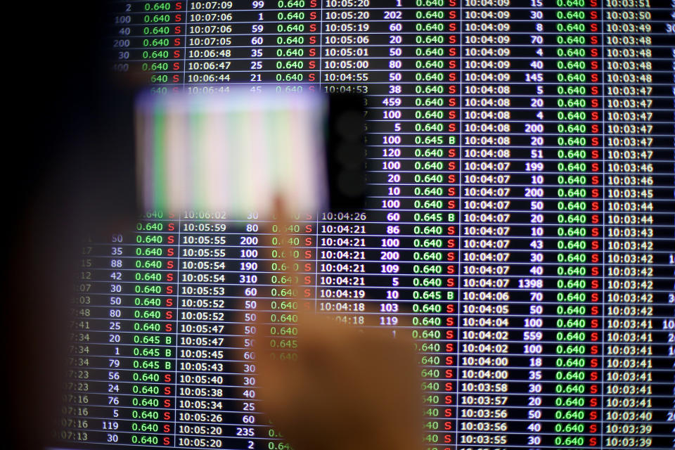 A person is pointing at a screen displaying stock market data with various numbers and times