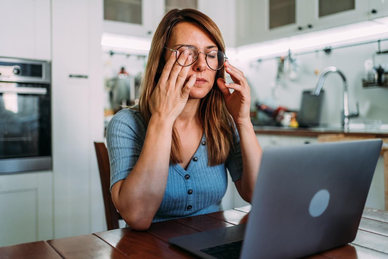 Overworked young businesswoman sitting in front of laptop and holding head.