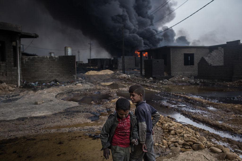 Two boys play outside their home in front of a burning oil well set on fire by fleeing Isis members on November 10, 2016 in Al Qayyarah, Iraq: Getty Images