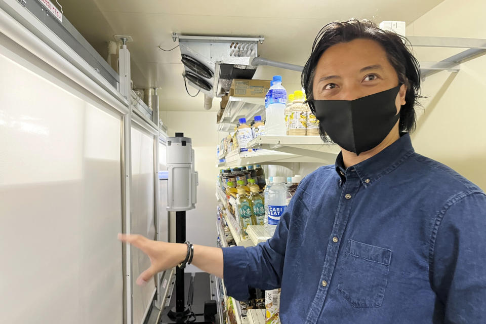 Telexistence CEO Jin Tomioka stands before his company’s robot, TX SCARA, center back, as it stocks drinks in the refrigerated section of a FamilyMart convenience store in Tokyo, Friday, Aug. 26, 2022. The robot can restock shelves with up to 1,000 bottles and cans a day. (AP Photo/Yuri Kageyama)