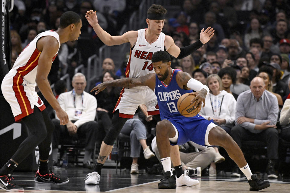 Los Angeles Clippers forward Paul George (13) loses his balance driving against Miami Heat guard Tyler Herro (14) and forward Jamal Cain, left, during the first half of an NBA basketball game, Monday, Jan. 1, 2024 in Los Angeles. (AP Photo/Alex Gallardo)