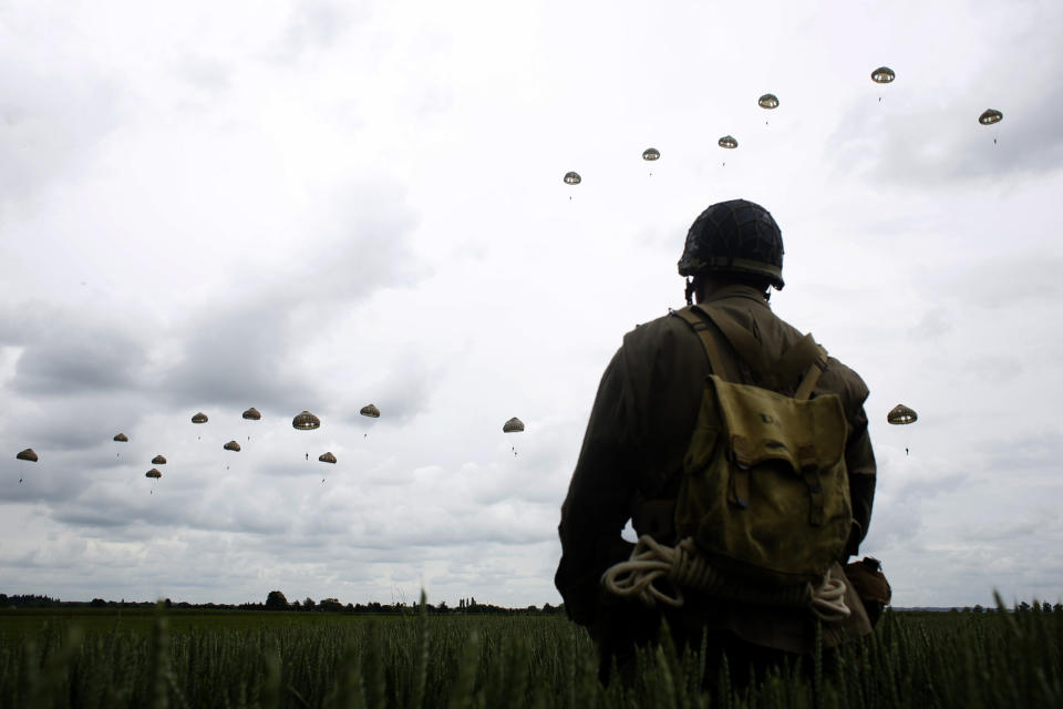 FILE - In this Wednesday, June 5, 2019 file photo, a WWII enthusiast watches French and British parachutists jumping during a commemorative parachute jump over Sannerville, Normandy, France. In sharp contrast to the 75th anniversary of D-Day, this year's 76th will be one of the loneliest remembrances ever, as the coronavirus pandemic is keeping nearly everyone from traveling. (AP Photo/Thibault Camus, File)