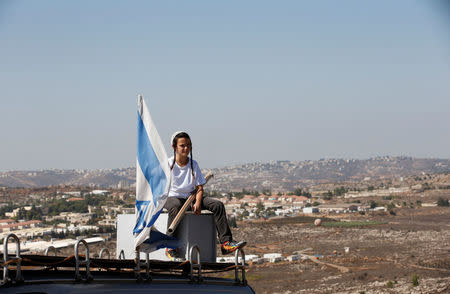 A boy sits near an israeli flag atop the roof of a vehicle at the entrance to the Jewish settler outpost of Amona in the West Bank, during an event organised to show support for Amona which was built without Israeli state authorisation and which Israel's high court ruled must be evacuated and demolished by the end of the year as it is built on privately-owned Palestinian land, October 20, 2016. REUTERS/Ronen Zvulun
