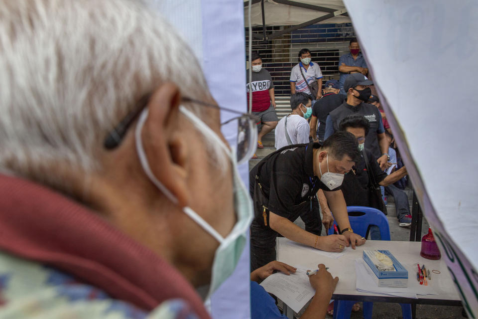 In this Thursday, March 19, 2020, photo, Muay Thai boxing fighters and officials gather at a makeshift screening facility outside Rajadamnern boxing stadium in Bangkok, Thailand. Kickboxing aficionados came from all over Thailand to attend a major Muay Thai tournament at Bangkok's indoor Lumpini Stadium on March 6, 2020. Dozens or more went home unknowingly carrying the coronavirus. For most people the new COVID-19 coronavirus causes only mild or moderate symptoms, but for some it can cause more severe illness. (AP Photo/Gemunu Amarasinghe)