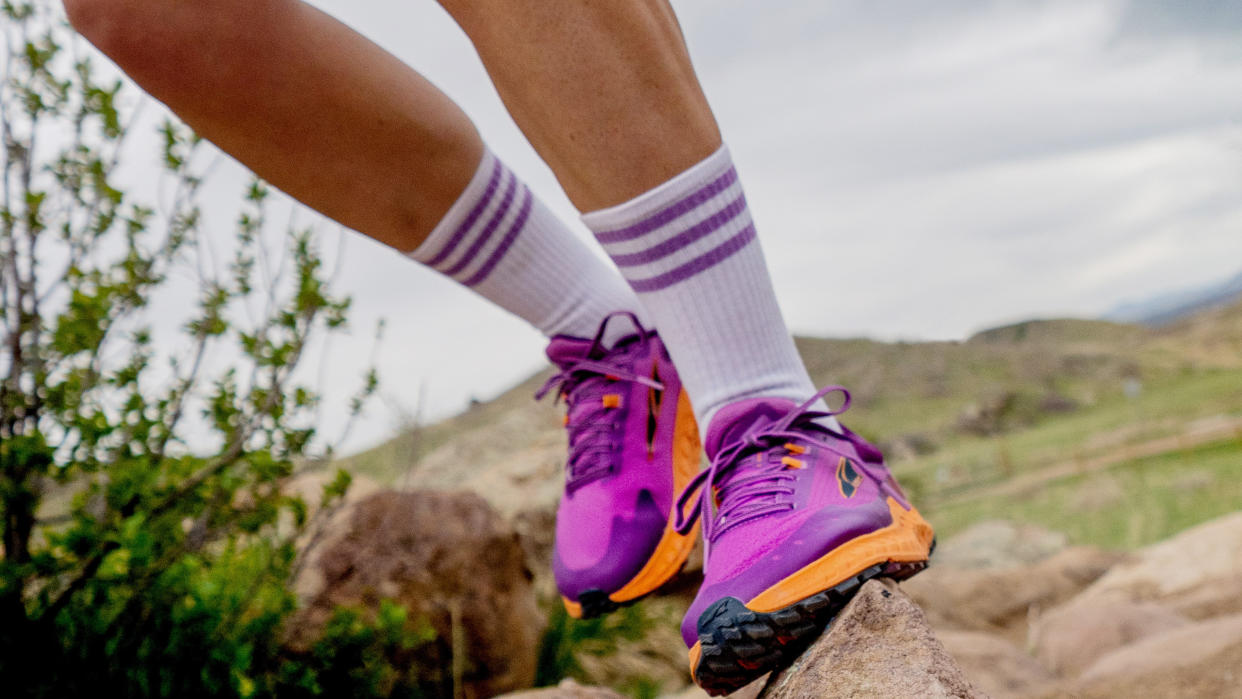  Person running on rocky trail wearing pink and orange Altra shoes 