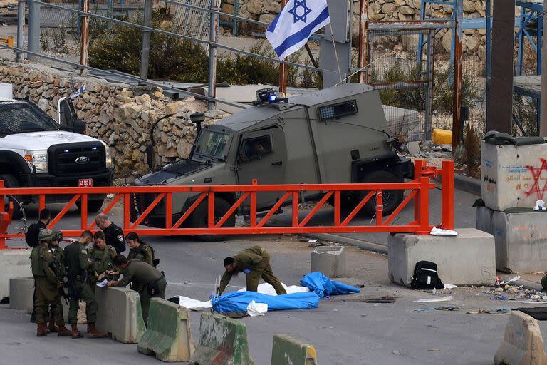 Fuerzas de seguridad israelíes se reúnen junto a dos cadáveres cubiertos en un puesto de control en la entrada norte de la ciudad ocupada de Hebrón, en Cisjordania, el 17 de noviembre de 2023. 