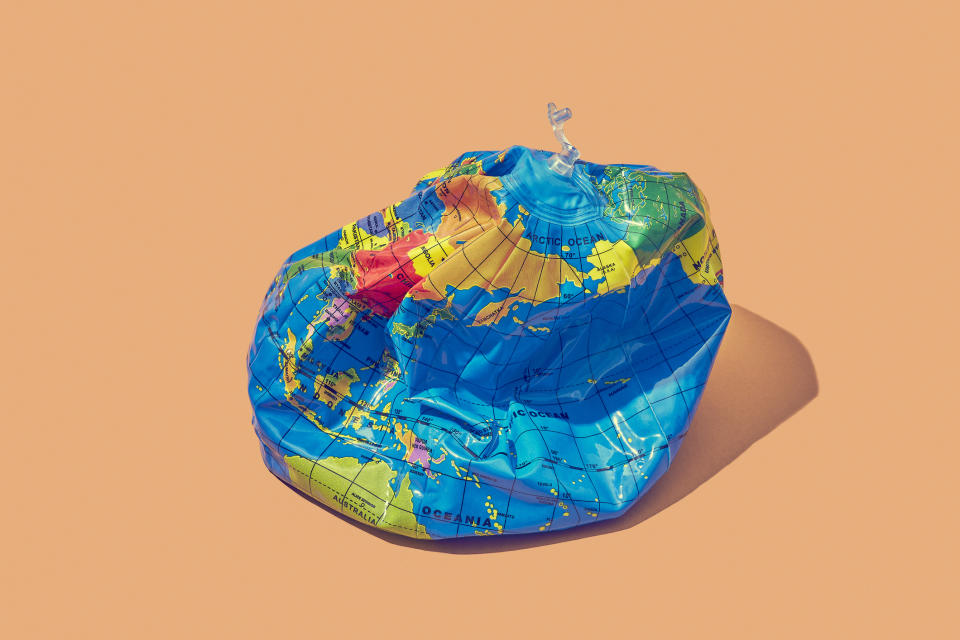 An inflatable globe that has deflated to symbolise a deflated economy. The globe is bright blue and has an unplugged air vent. It's on a peach background.
