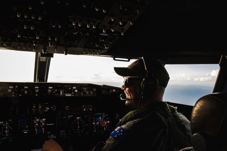 A man sits in the cockpit of a P-8A Poseidon plane looking out at the open ocean.