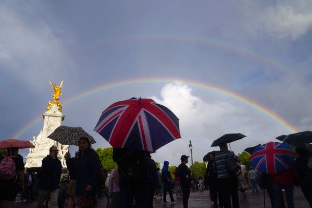 A double rainbow is seen, as members of the public who are carrying union flag umbrellas gather outside Buckingham Palace