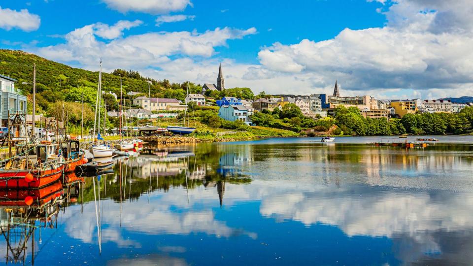 pier at the port of clifden at high tide, boats anchored with mirror reflection in the water, sunny spring day with a blue sky and abundant white clouds in clifden, ireland