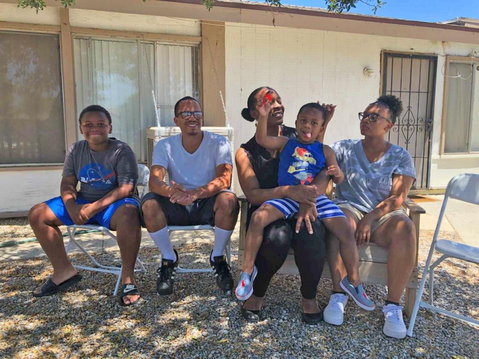 A family of five sitting in the shade outside a home