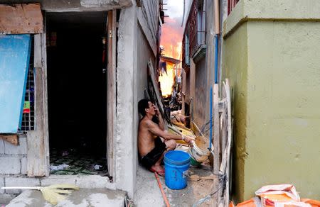 A man sits in a narrow alley as his house burns in Muntinlupa, Metro Manila, Philippines, June 4, 2018. REUTERS/Erik De Castro
