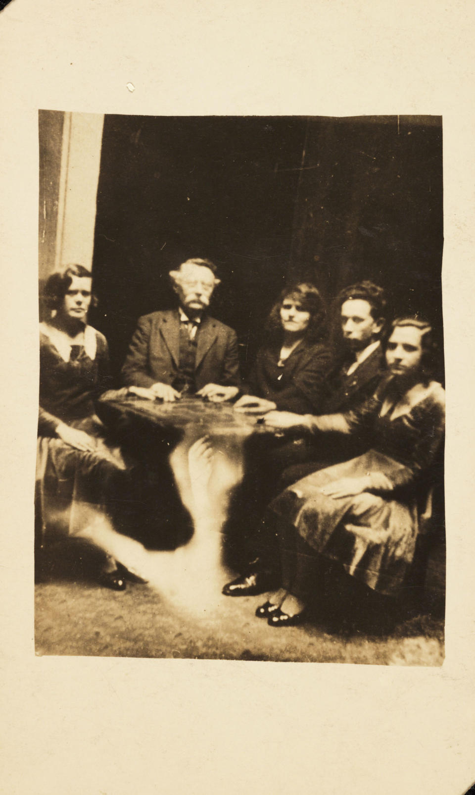 <p>A group gathered at a seance with a ghostly arm lifting the table. </p>