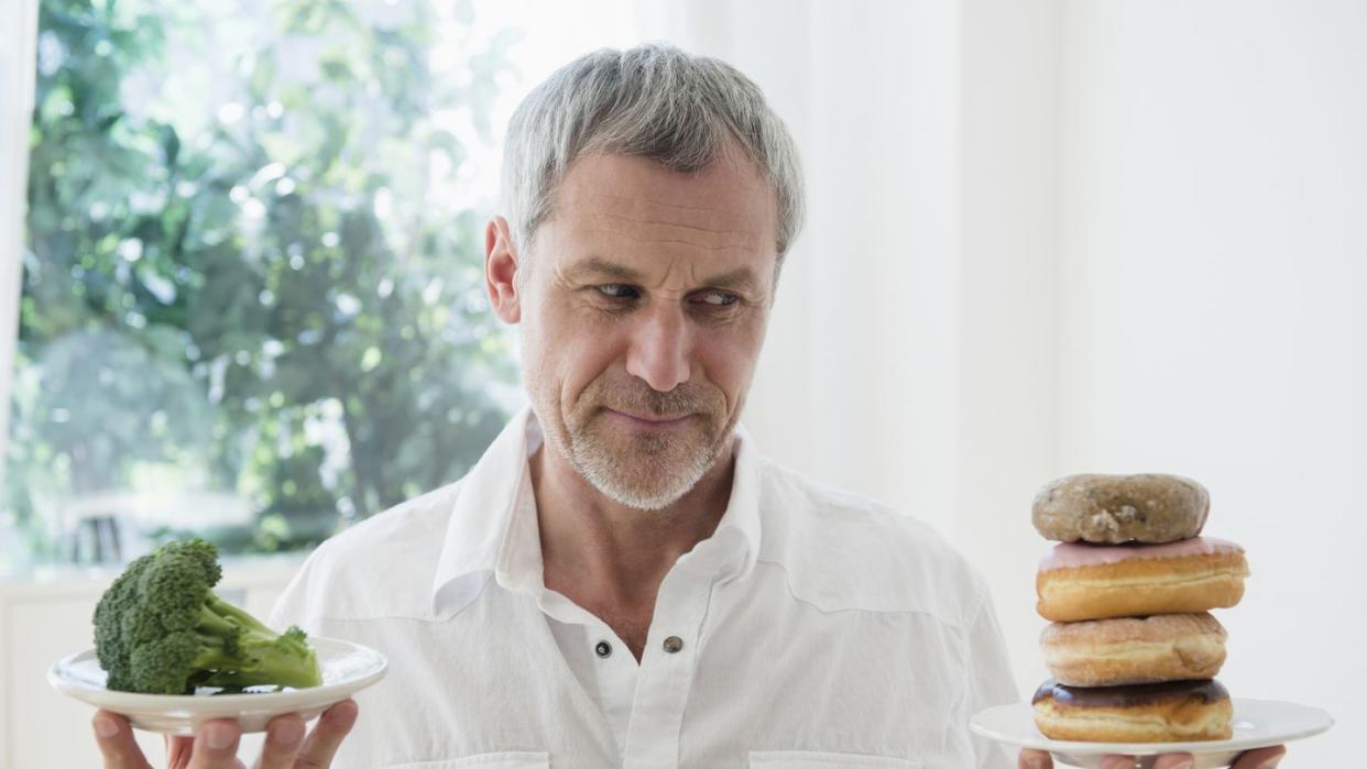 older caucasian man choosing between broccoli and donuts