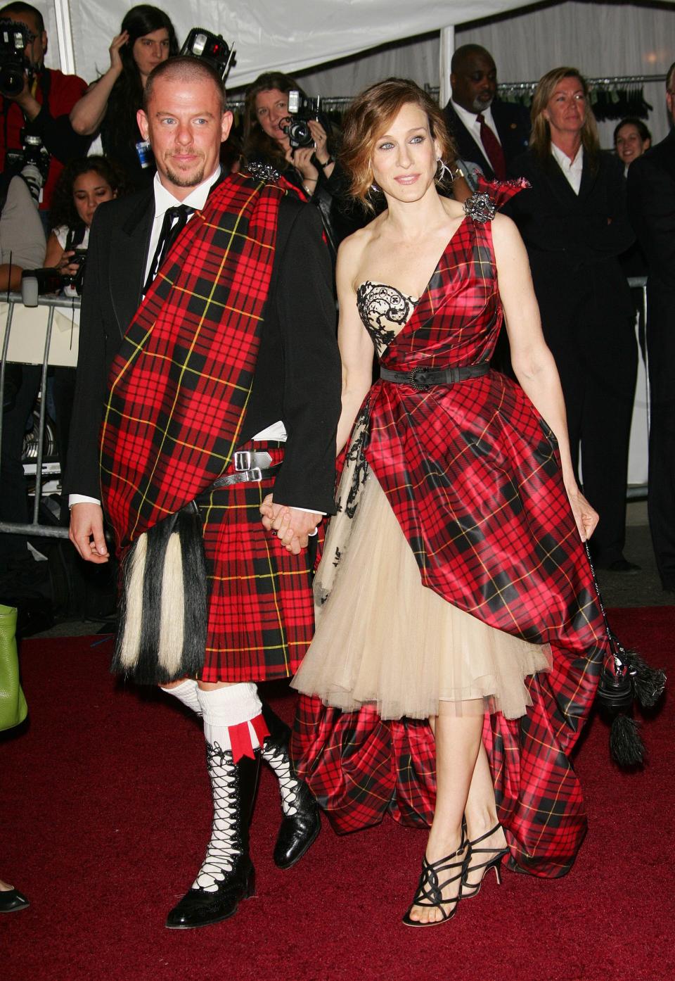 Alexander McQueen in a red plaid sash over his suit jacket and a red plaid kilt. Sarah Jessica Parker in a nude tulle strapless dress with a lace bustier and red plaid sash forming one arm strap and being belted before flowing over the dress to the ground.