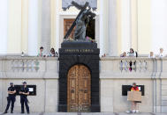 In this Aug. 2, 2020 taken photo an LGBT rights activist draped in a rainbow flag holds a sign in front of a church in Warsaw, Poland. LGBT people are choosing to leave Poland amid rising homophobia promoted by President Andrzej Duda and other right-wing populist politicians in power. On Thursday, with Duda to be sworn in for a second term as president, some LGBT people have already left Poland or are making plans to leave. (AP Photo/Czarek Sokolowski)