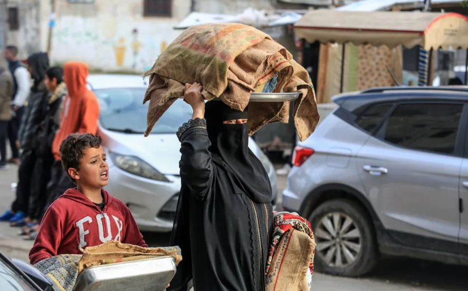 Người phụ nữ Palestine đội thứ gì đó trên đầu khi cuộc sống hàng ngày tiếp tục dưới sự tấn công của Israel ở Rafah, Gaza