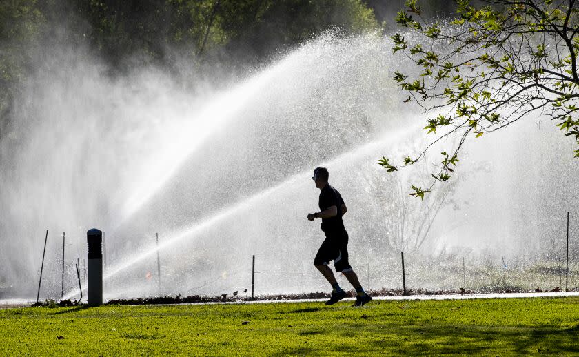 RIVERSIDE, CA - SEPTEMBER 22, 2022: A jogger runs past the mist from afternoon sprinklers near The Meadow at Ryan Bonaminio Park on September 22, 2022 in Riverside, California.The first day of fall will be met with increasing temperatures as another heat wave makes its way to Southern California. (Gina Ferazzi/Los Angeles Times)