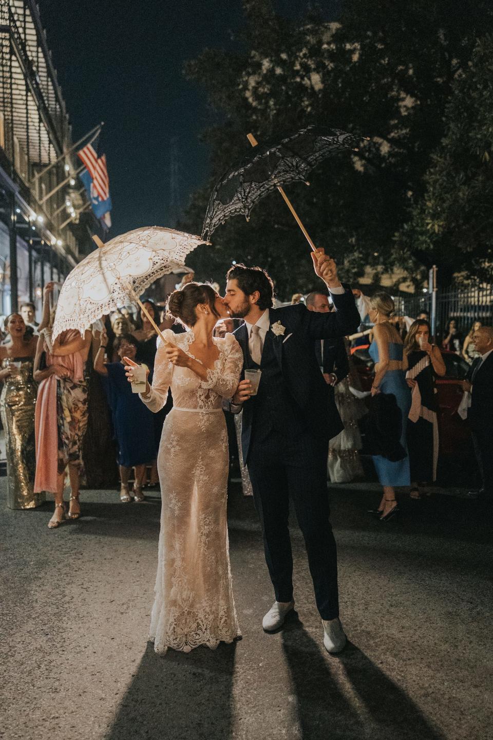 A bride and groom kiss holding umbrellas as they do a second line parade.