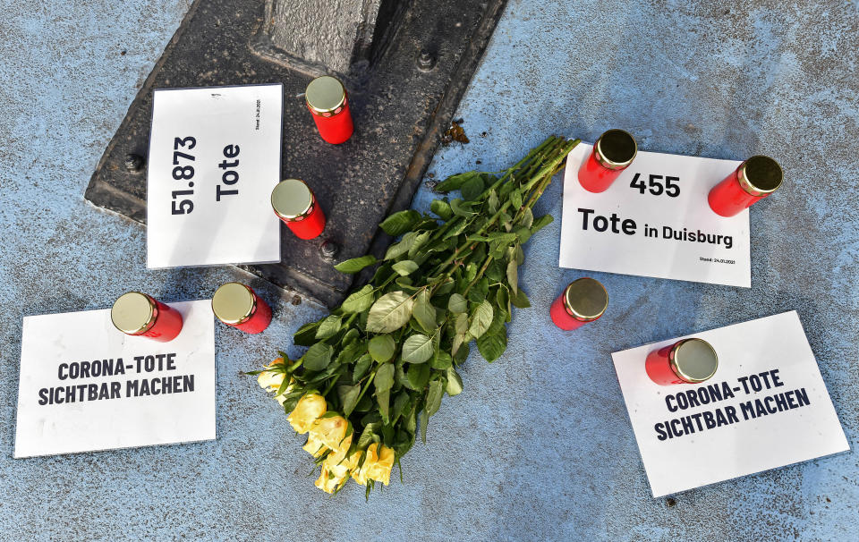 Candles and flowers to honor those who died with or of COVID-19 are set at a main shopping street in Duisburg, Germany, Monday, Jan. 25, 2021. Notes reading 'make corona deaths visible', '51.873 deaths' and '455 deaths in Duisburg'. (AP Photo/Martin Meissner)