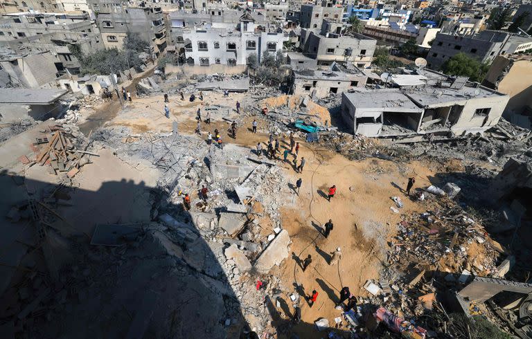 Un incendio mientras los equipos de rescate palestinos trabajan bajo los escombros de un edificio derrumbado este sábado tras un ataque israelí, en Khan Yunis, en el sur de la Franja de Gaza, en medio de las batallas en curso entre Israel y los islamistas palestinos. grupo Hamás. (Photo by Mahmud HAMS / AFP)