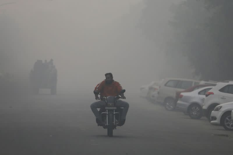 Man rides a motorbike along a road shrouded in smog in Noida