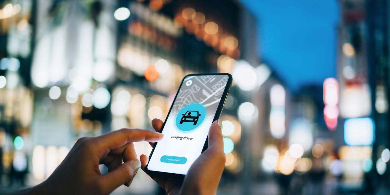 close up of young woman using mobile app device on smartphone to arrange a taxi ride in downtown city street, with illuminated city traffic scene as background