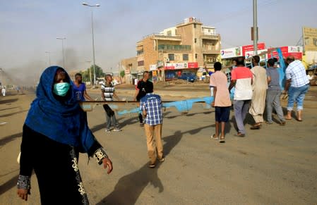 A woman walks past Sudanese protesters erecting a barricade on a street and demanding that the country's Transitional Military Council hand over power to civilians in Khartoum