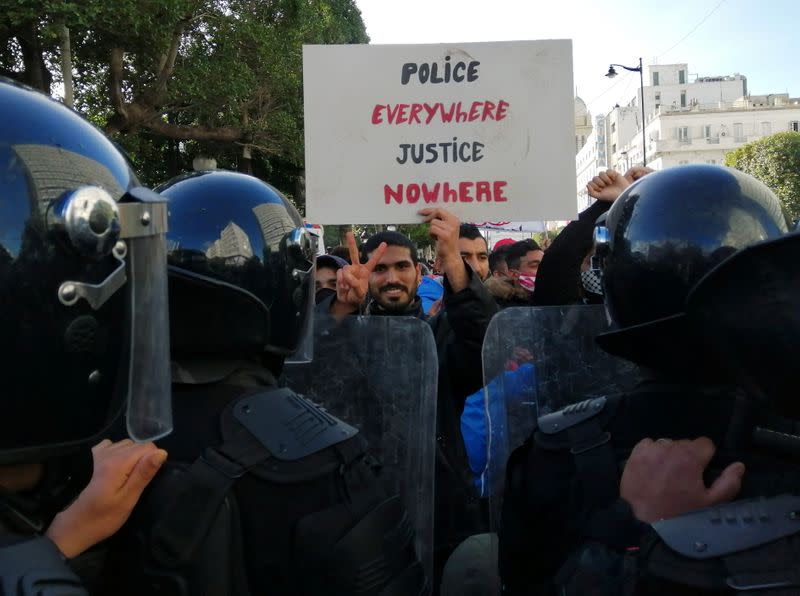 Police officers stand guard as a demonstrator gestures and carries a placard during an anti-government protest in Tunis