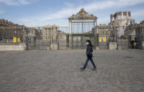 FILE - In this April 21, 2020 file photo, a woman walks past the closed Chateau de Versailles, west of Paris. Iconic sites that are among some of France's biggest tourist draws won't reopen when the country lifts most of its coronavirus restrictions next week. Neither the Louvre Museum, the Eiffel Tower nor the Versailles Palace will be reopening next week when France lifts many of its remaining coronavirus lockdown restrictions. (AP Photo/Michel Euler, File)