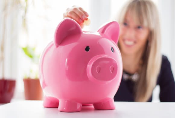 A woman adding coins to her piggy bank.