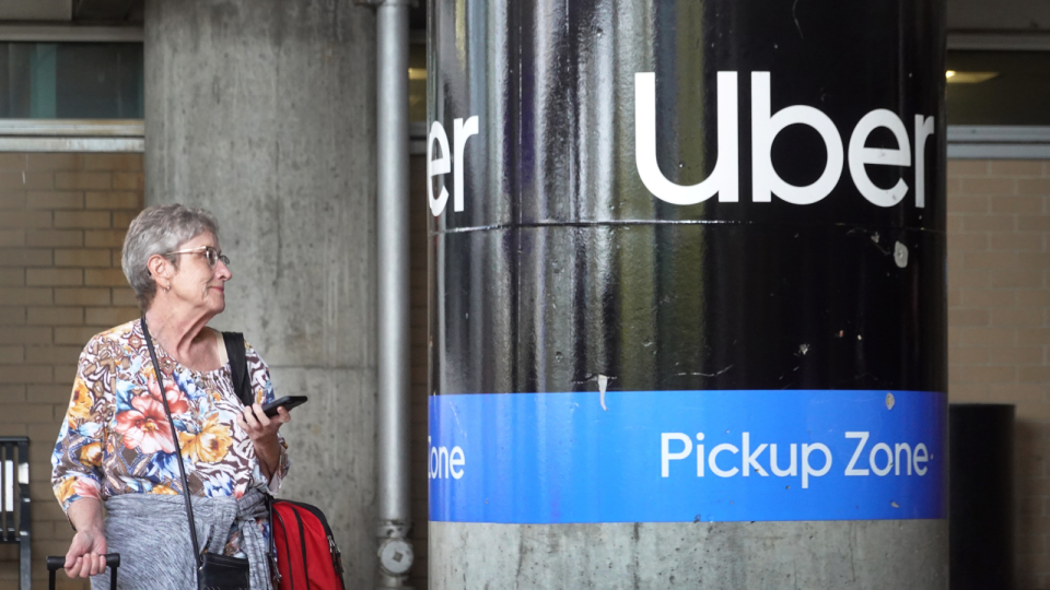 An elderly woman stands at an Uber pickup zone.