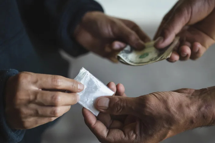 Hands of man with money buying dose of cocaine or heroine from a dealer.