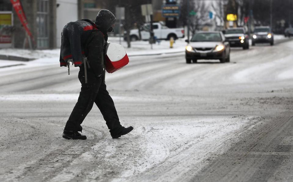 A man carries his belongings across the snow-covered intersection of West Clearwater Avenue and South Union Street in Kennewick.