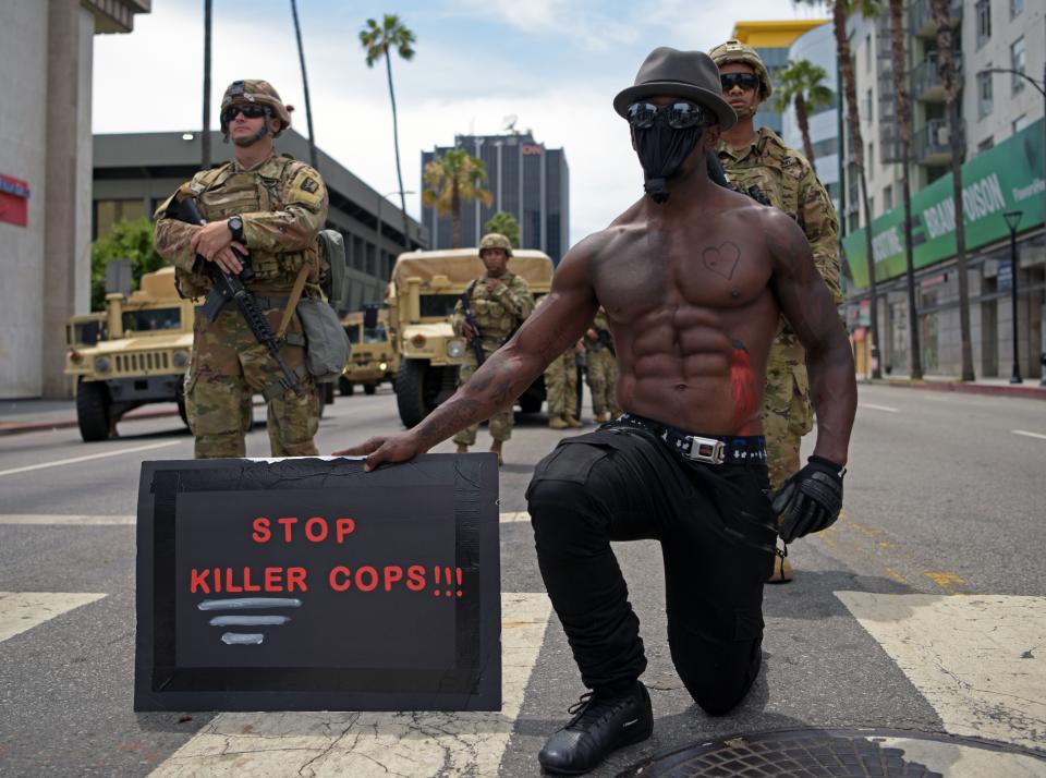 <i>A protester kneels as he holds a placard that says "Stop killer cops!!!!" in front of a row of Army National Guard troops during a June 2 demonstration in Hollywood, California.</i>