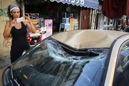 A woman takes a photo with her mobile phone of a car damaged when the remains of a rocket intercepted by Israel landed in a Tel Aviv neighbourhood July 10, 2014. REUTERS/Finbarr O'Reilly